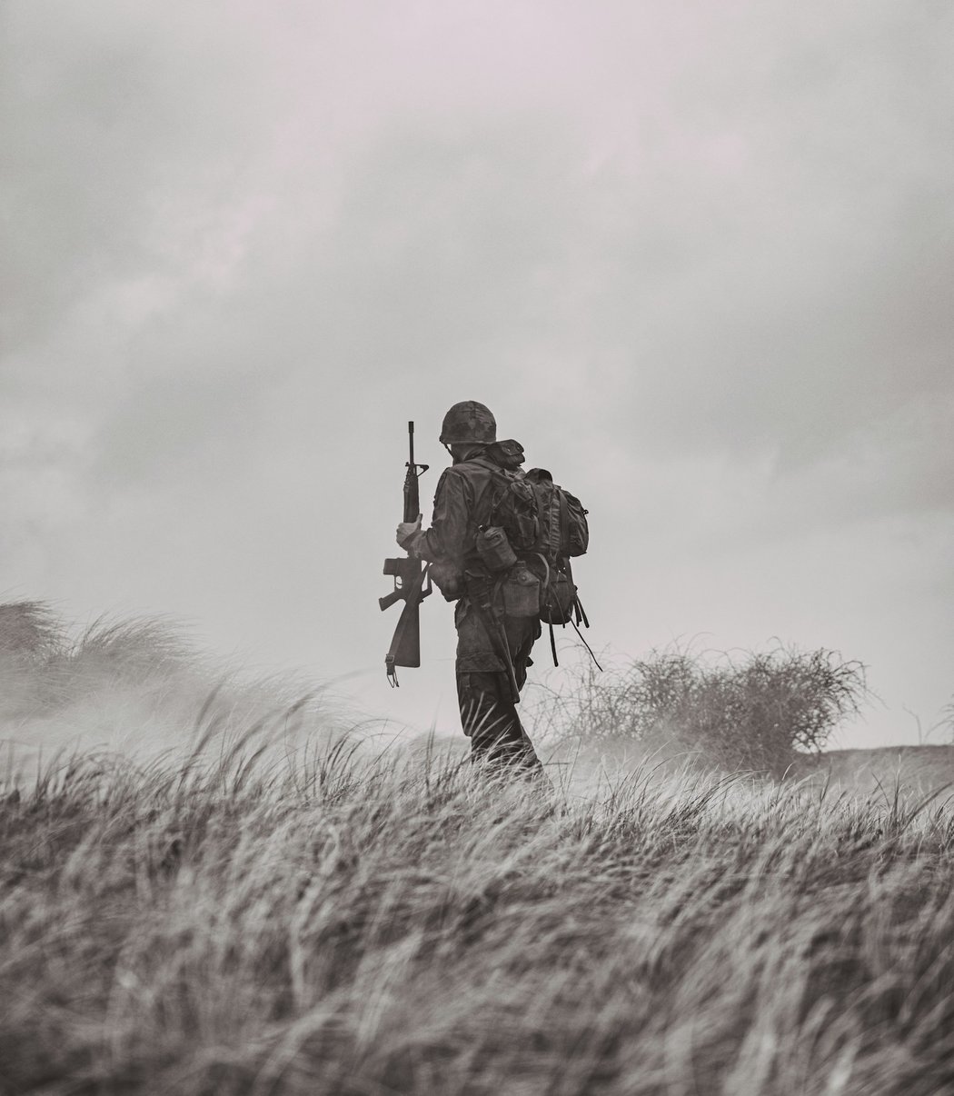 ライフルを背負って草原を歩く兵士のモノクロ写真