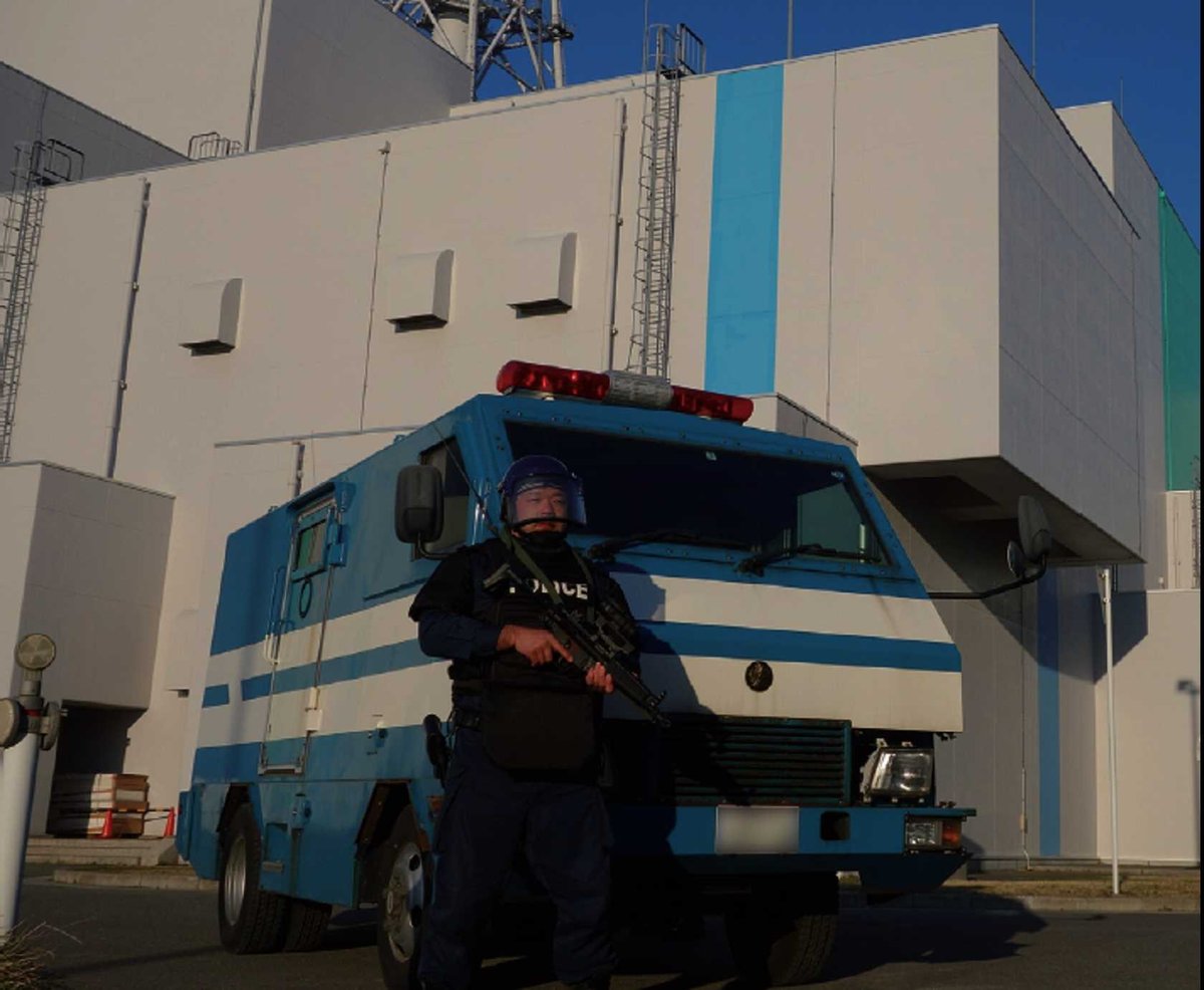 紺の活動服に黒の防弾ベストとヘルメットで小銃を持ち、装甲車の前で警戒する警察官